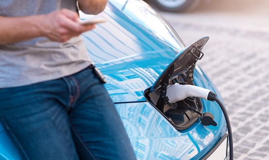 Man holding smartphone while charging car Man charging electric car while holding smartphone