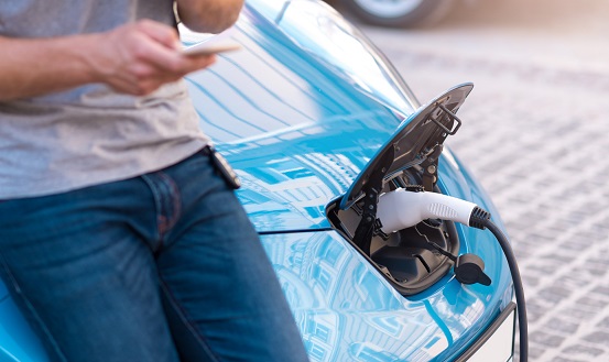 Man charging electric car while holding smartphone